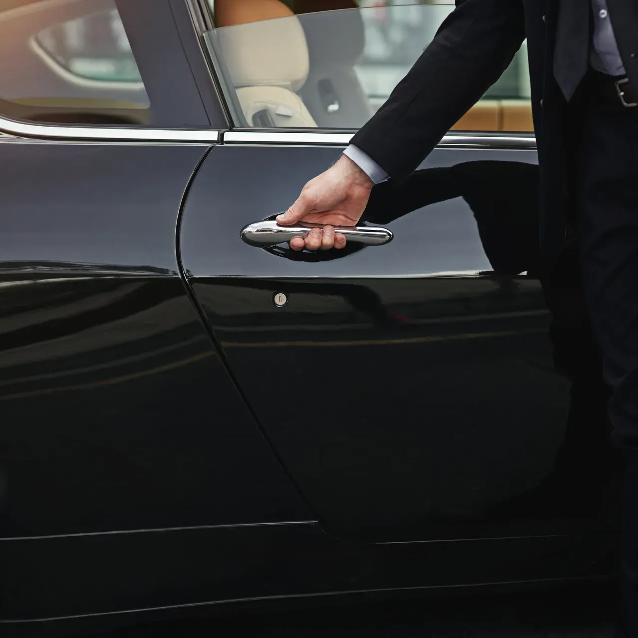 Chauffeur en costume ouvrant la portière d'une berline noire